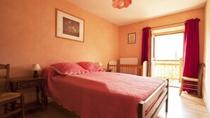 Ein Schlafzimmer mit Bett, Nachttisch, Sessel, einem Fenster mit Vorhängen und Blick ins Freie.