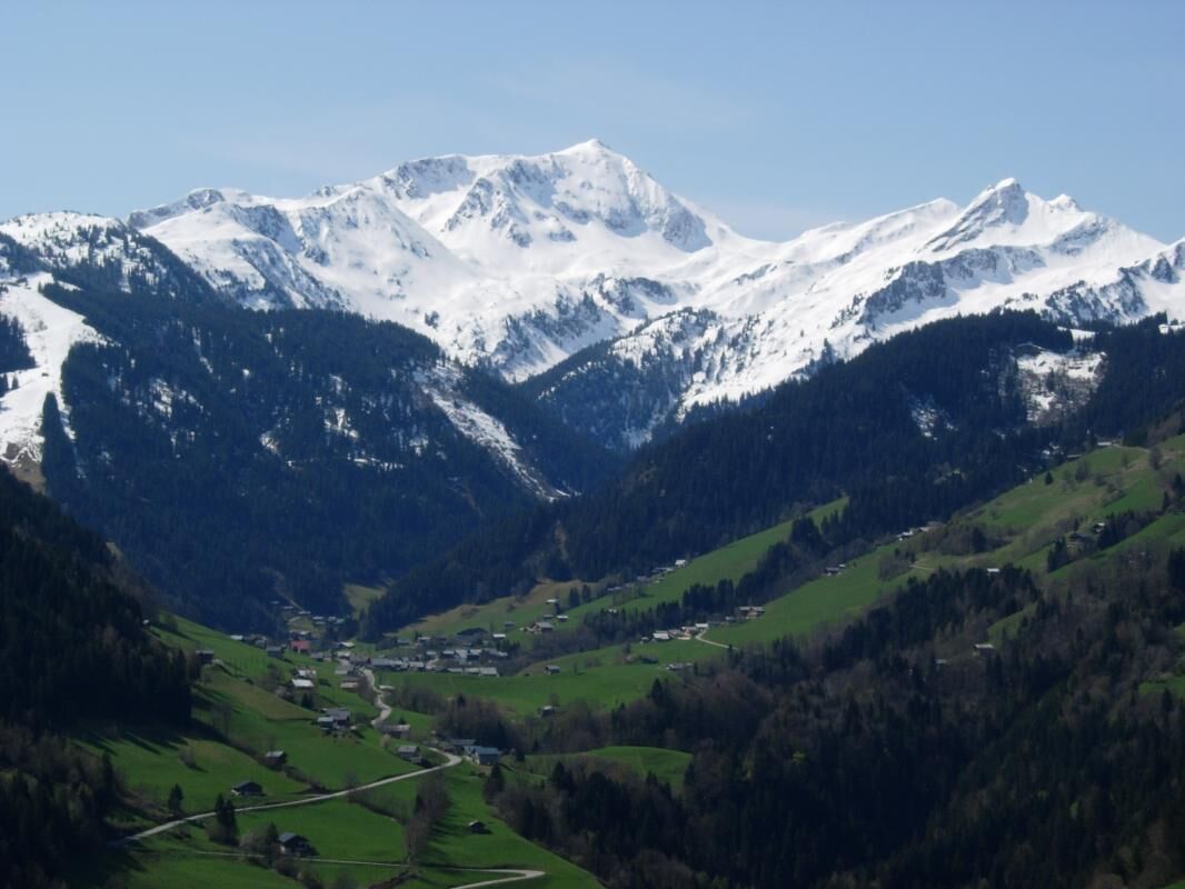 Paisagem montanhosa com picos nevados e um vale com edifícios dispersos.