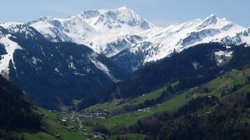 Paisagem montanhosa com picos nevados e um vale com edifícios dispersos.