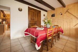 Un coin repas avec une table en bois dressée pour quatre personnes, un vase rempli de fleurs et un mur en bois avec une poutre de plafond inclinée.