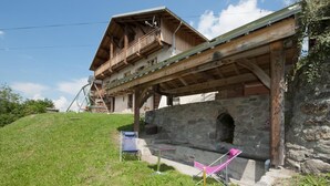 Eine traditionelle Holzhütte mit Balkon, Steinmauern und einer grünen Böschung.