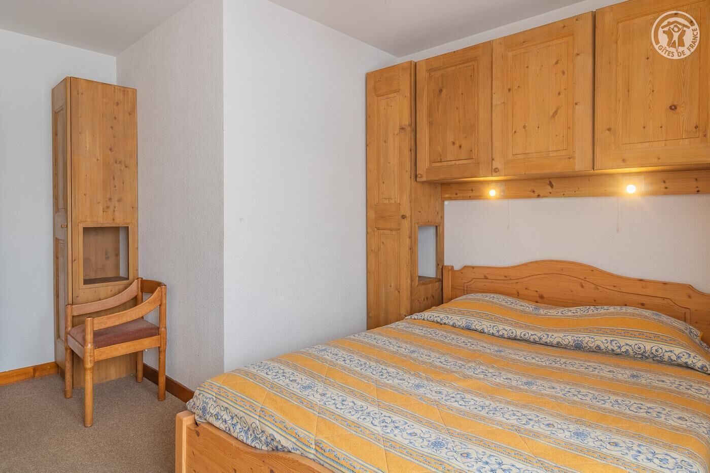 A bedroom with a wooden bed, a wooden chair, and built-in wooden cabinets.
