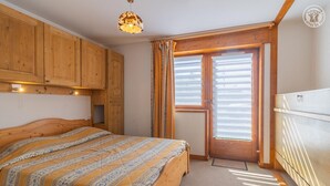 Un dormitorio con cama de madera, una lámpara en el techo, una ventana con persianas y una puerta.