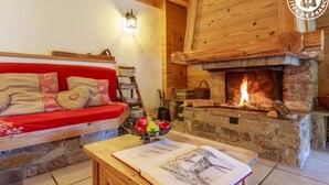 Una sala de estar acogedora con chimenea de piedra, un sofá rojo con cojines estampados y una mesa con un cuenco de fruta y un libro.