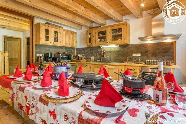 A dining area with a long table set for a meal, wooden cabinets, and a kitchen in the background.