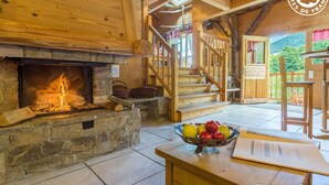Un interior rústico de madera con chimenea de piedra, una escalera de madera y un comedor con frutero.