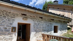 A stone building with a wooden door, a small window, and a wooden deck with benches. - Chalet LE Char - Gite "LE Plan" (LA GIETTAZ)