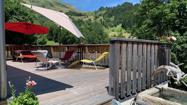A wooden deck with lounge chairs and umbrellas, surrounded by a wooden fence and a small pond. - Chalet LE Char - Gite "LE Plan" (LA GIETTAZ)