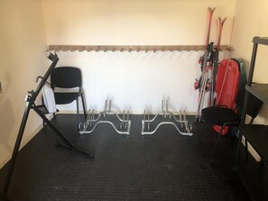 A garage with a black floor, a white wall, and a wooden beam at the top. There are two metal racks for skis and a black chair.