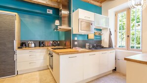 A modern kitchen with white cabinets, a wooden countertop, and a blue accent wall. - Clos DES Platanes-cote Figuier (BRISON SAINT INNOCENT)
