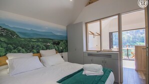 Une chambre avec un grand lit, une couvre-lit verte, une table de chevet, un miroir et une vue sur l’extérieur.