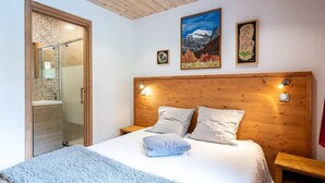 A bedroom with a wooden headboard, a bed with two pillows, a fluffy rug, and a painting of a mountain scene. - L'attrape-rêves - Bessans (BESSANS)