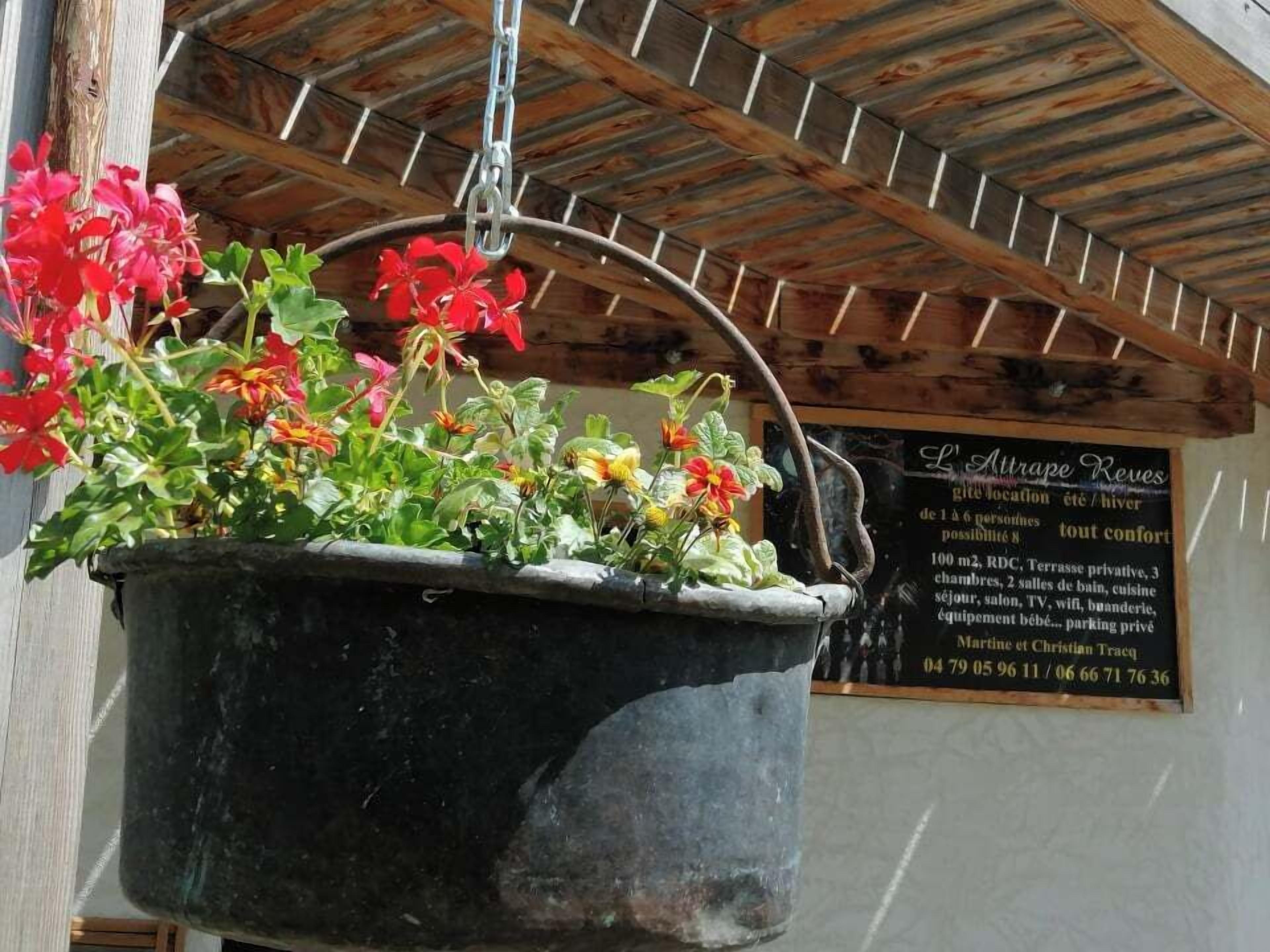 Um vaso de flores pendurado com flores vermelhas e amarelas, teto de madeira e uma placa com texto em francês.