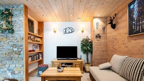 A cozy living room with a stone wall, wooden shelves, a TV, a coffee table, a sofa, and a plant. - L'attrape-rêves - Bessans (BESSANS)