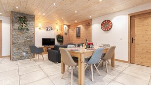 A modern living room with a stone wall, wooden ceiling, and a dining area with a wooden table and chairs. - L'attrape-rêves - Bessans (BESSANS)