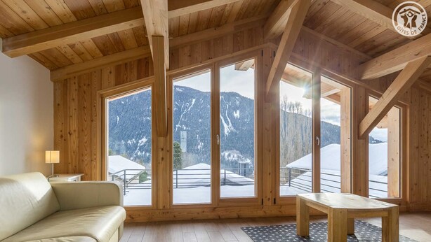 A wooden interior with a sofa, a table, and large windows offering a mountain view.