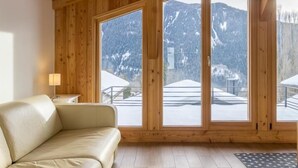 A wooden interior with a sofa, large windows, and a view of snow-covered mountains.