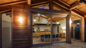 A modern kitchen with wooden cabinets, a dining area with chairs, and a large glass door leading to an outdoor deck.