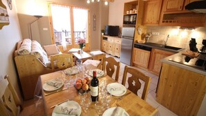 A cozy kitchen with wooden cabinets, a dining area with a table set for a meal, and a balcony with a view. - Chez Marie - Albiez Montrond (ALBIEZ MONTROND)