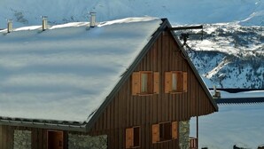 A wooden chalet with a sloped roof, stone walls, and multiple chimneys. It is surrounded by snow-covered mountains and a clear sky. - Chez Marie - Albiez Montrond (ALBIEZ MONTROND)