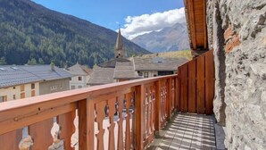 A balcony with a wooden railing, a stone wall, and a view of a mountain and a church. - LA Pastorale - LE Genepi (VAL CENIS)