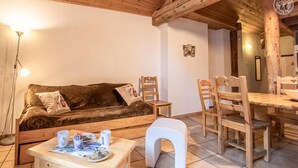 A cozy room with a wooden sofa, a small table with a plate and cups, and a dining area with wooden chairs and a table. - LA Pastorale - LE Genepi (VAL CENIS)