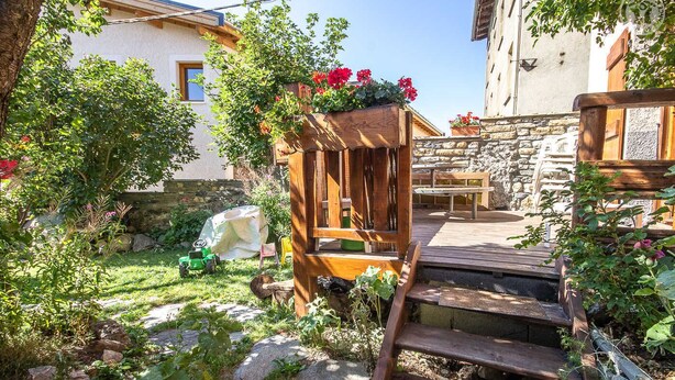 A wooden deck with a bench, a small garden with a wooden structure, and a stone wall. - LES Pinatsotes - Aussois (AUSSOIS)