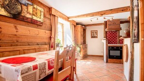 A rustic wooden dining area with a table set for two, a kitchen with a red tiled backsplash, and wooden beams on the ceiling. - LES Pinatsotes - Aussois (AUSSOIS)