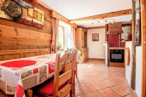 A wooden interior with a dining table set for two, a kitchen area with a stove, and a red tiled floor.