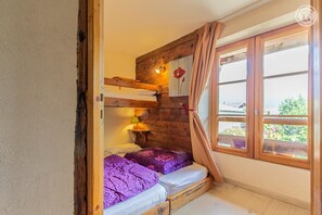 A small, cozy room with a bunk bed, a window with curtains, and a view of greenery outside.