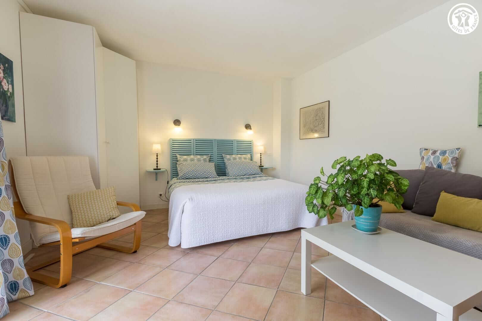 A bedroom with a bed, bedside tables, a chair, a sofa, and a potted plant.