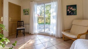 Une pièce avec une porte en bois, une chaise, un radiateur, une grande fenêtre avec des rideaux et un tableau accroché au mur.