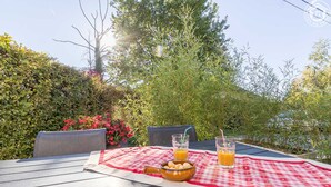 Un espace de restauration en plein air avec une table dressée pour deux personnes, agrémentée d’une nappe à carreaux rouges et blancs, de deux verres de jus d’orange et d’un bol de collations.