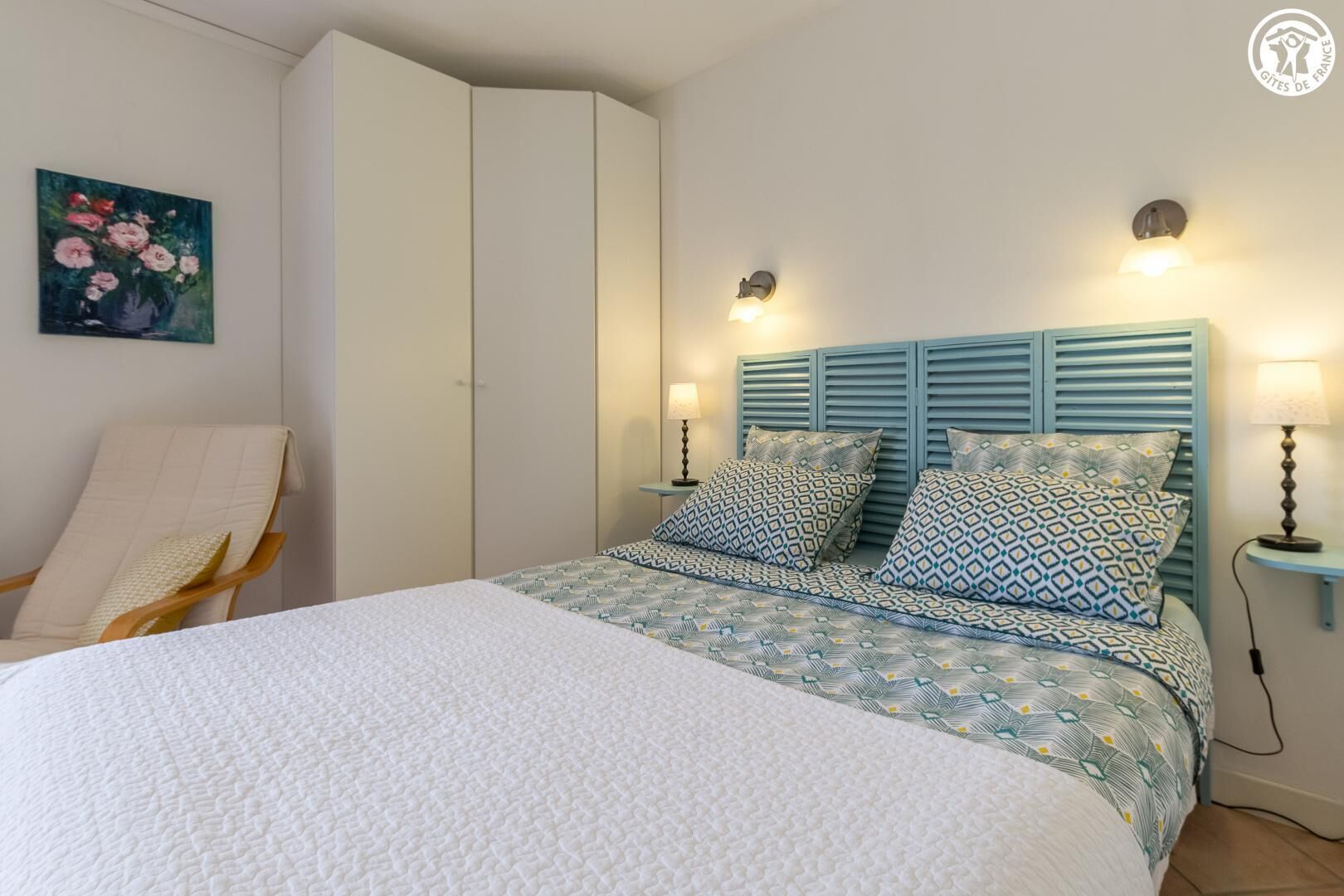 Un dormitorio con una cama, dos mesitas de noche, una silla y un armario.