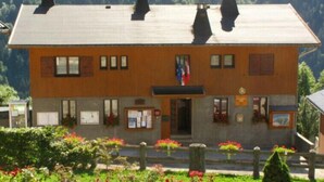 Ein zweistöckiges Gebäude mit Flachdach, mehreren Schornsteinen und einer Flagge davor.