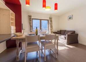 A modern, well-lit room with a dining table set for two, a sofa, and a window with a view.