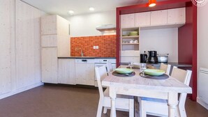 A modern kitchen with white cabinets, a red backsplash, and a dining area with a wooden table and chairs. - LA Lauziere - Montsapey (MONTSAPEY)