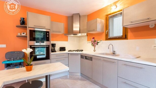A modern kitchen with a built-in oven, microwave, and gas stove. There is a dining area with a table and chairs, and a small potted plant.