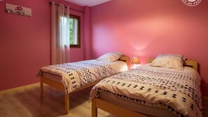 A bedroom with two beds, a window with curtains, and a lamp.