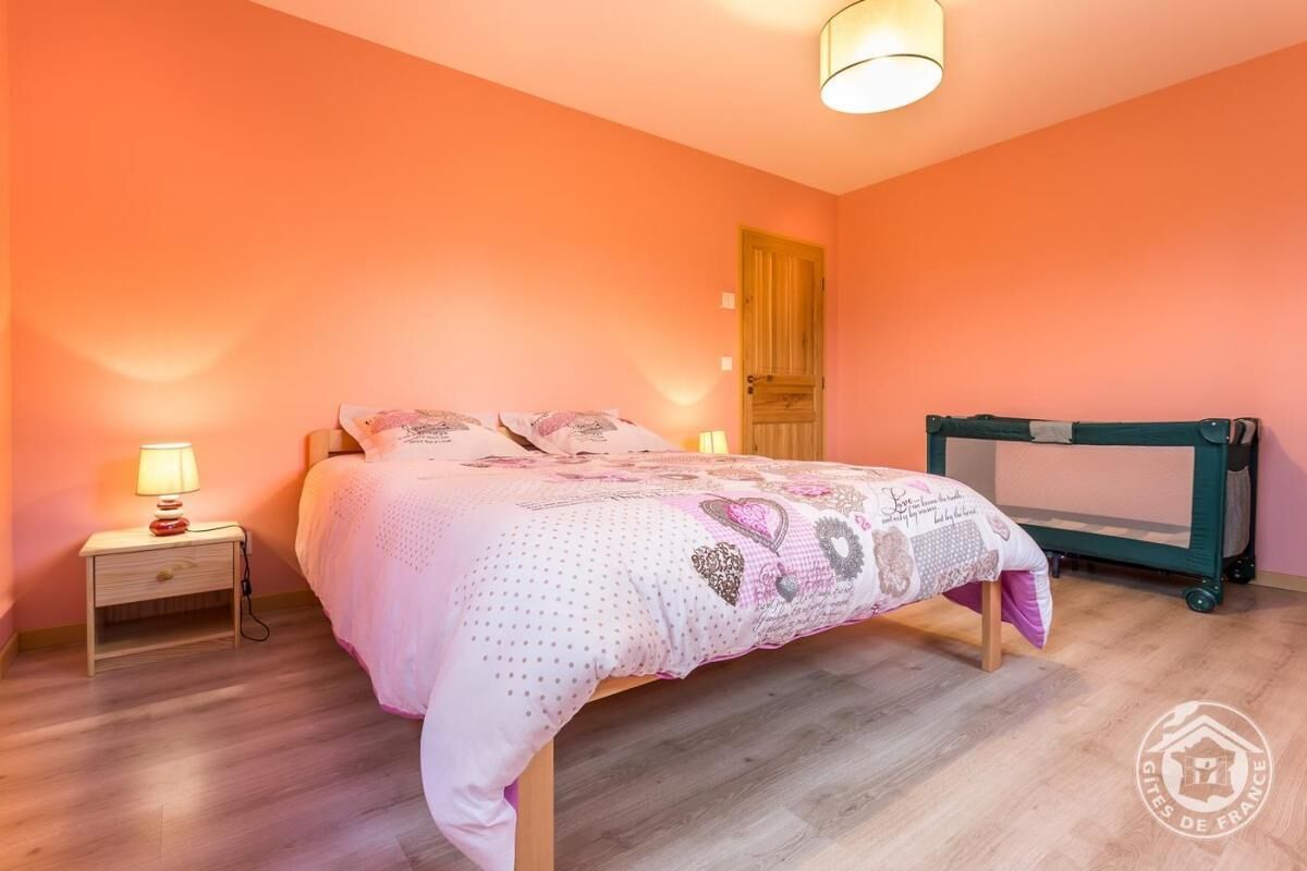 A bedroom with a bed, a nightstand with a lamp, a wooden door, and a green trolley.
