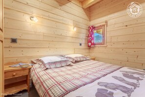 A cozy wooden cabin bedroom with a bed, bedside tables, and a window with a red curtain.