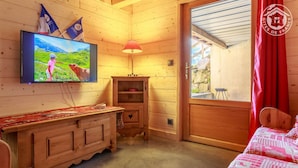 A cozy room with a wooden cabin interior, a television mounted on the wall, a small wooden cabinet, and a bed with a red and white patterned bedspread.