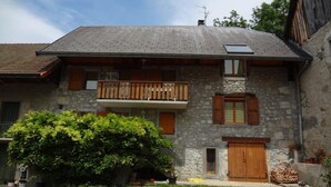 Ein zweistöckiges Steinhaus mit Balkon, Holzh shutters und einem kleinen Garten.