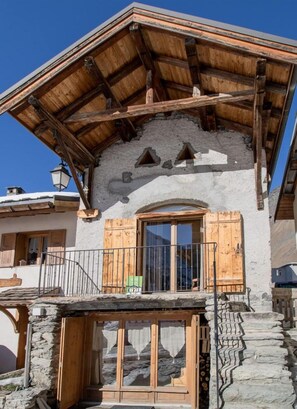 Una cabaña tradicional con base de piedra, balcón de madera y puerta de madera.