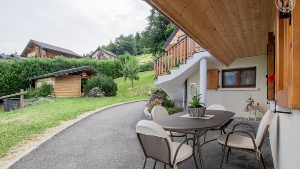 A patio with a table and chairs, surrounded by a wooden fence and greenery.