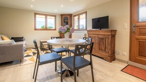 A modern kitchen with a dining table, chairs, and a TV. There is a sofa and a window with a view.