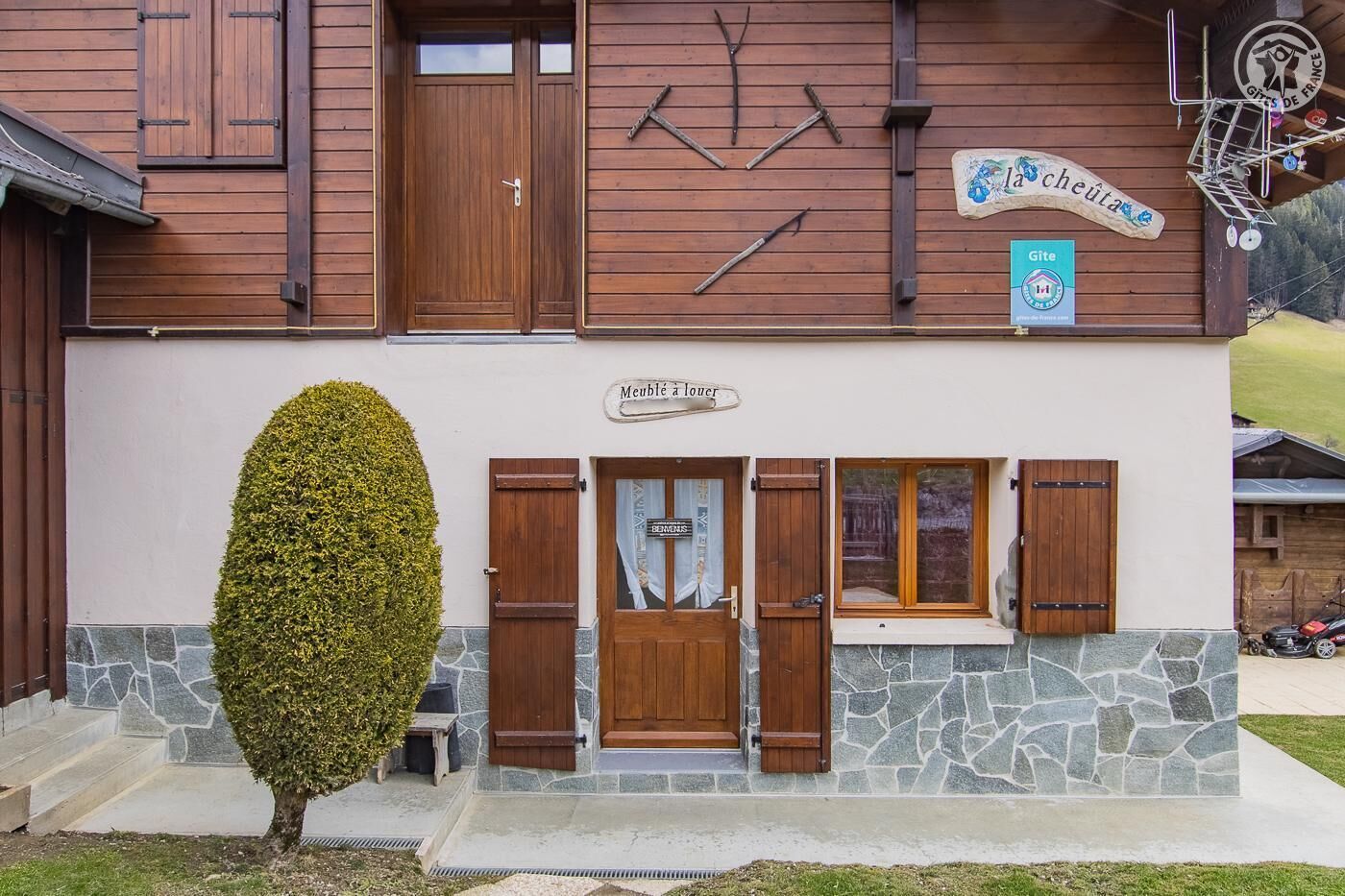 A building with a wooden facade, a stone base, and a sign reading "Meuble à louer".