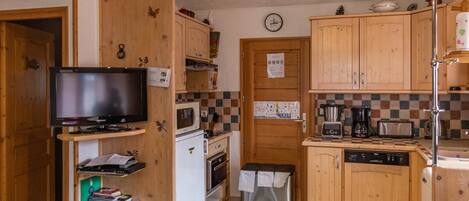 A compact kitchen with wooden cabinets, a microwave, a stove, a sink, and a small refrigerator.