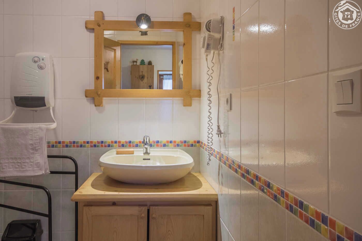 Un baño con lavamanos blanco, armarios de madera, un espejo y una ducha.