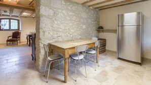A rustic kitchen with a stone wall, wooden table, and stainless steel refrigerator. - LE Gite DE Myans - Myans (MYANS)